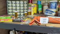Photo showing four shelves of assorted household and hardware items including sprays like OFF insect repellent and Strike ant bait, small hardware components in a drawer organizer, a stapler, and small tools.