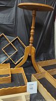 Photo showing wooden accent table with turned pedestal and tripod base standing behind interlocking wooden shelves.