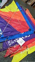 Photo showing vibrant kite sections in multiple colors with strings and rods arranged side by side on a table.