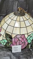 Photo showing lower side of stained glass pendant light with pink and green rose design, white/beige glass panels, and metal hardware on top.