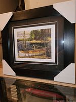 Framed fine art print titled 'The Canoe' by Tom Thomson inside black frame with corner protectors.