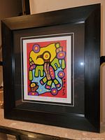 Photo of professionally framed fine art print by Christian Morrisseau titled "Thunderbird" showing vibrant Indigenous-inspired imagery, black frame, and white matting.