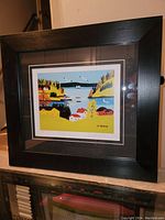Full view of the professionally framed Maud Lewis fine art print 'Sandy Cove' in black frame on a shelf.