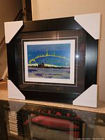 Full view of professionally framed Tom Thomson fine art print titled "Northern Lights." The frame is black wood with protective corner covers, showing the matted print inside.