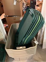 Six beige plastic storage bins stacked inside each other with six green lids stacked inside one bin.
