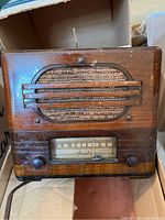 Front view of the antique wooden Phonola radio showing the speaker grille, horizontal wood bars, and front panel knobs.