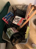 Bin full of assorted hand and garden tools including bolt cutters, pliers, manual jigsaw, hammers, toolboxes, and various handles.