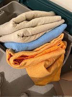 Five folded vintage blankets of various colors with satiny trim inside a storage bin.