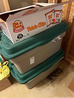 Two green-lidded plastic storage bins stacked, with a box of Old Dutch Potato Chips on top