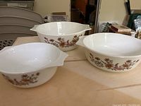 Three white glass Pyrex nesting bowls with country autumn brown and orange floral pattern shown side by side.