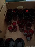 Top-down view inside a box showing 28 pieces of cranberry glassware including tall and short glasses, some stemmed and some stemless, deep red color.