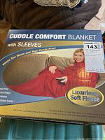 Box front showing Cuddle Comfort Blanket with Sleeves packaging and product features including soft fleece and hands-free warmth.