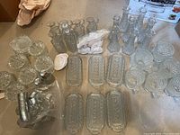 Full view of the lot showing all glass pieces including butter dishes, bottles, shakers, vases, cream & sugar containers and ashtrays on carpeted floor.