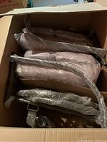 Open cardboard box containing multiple metal garden chair frames wrapped in bubble wrap and cushioned chair seats.