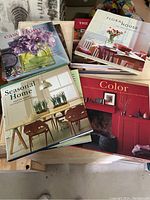 Top view of nine home decor coffee table books stacked and spread on wooden table showing covers of several titles.