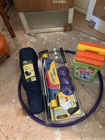 Photo of purple hula hoop, Pro Golf Series golf set with clubs and balls in packaging, and navy blue junior folding chair in carrying bag on floor.