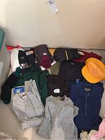 Overview photo of men's clothing including long sleeve tops, short sleeve tops, socks, papal hats, yellow cap, and mitts laid out on floor