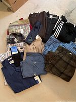 Overall view of all clothing items laid out, showing shirts, pants, pyjamas, sweaters, pullovers, and ties all new with tags.