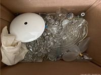 Box of assorted chandelier parts including glass shades, crystal prisms, and frosted bulb covers.