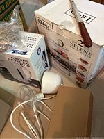 Photo showing boxed Libbey covered cake plate and boxed Hamilton Beach cordless electric kettle along with a white kettle base and cardboard box.