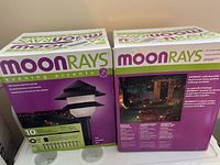 Two sealed boxes of Moonrays Evening Accents solar landscape lights, each box labeled to contain 10 lights, 4 watt brightness, 50 feet cable, with product images and specifications.