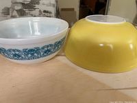 Two Pyrex mixing bowls side by side, one solid yellow and one white with blue pattern