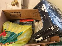 Box containing black stool, paint roller covers, sanding sponge, and plastic bag with supplies.