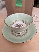 Cup placed on the matching saucer showing floral pattern and gold trim with the word 'Mere' inside the cup and on saucer center.