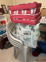 Stack of 4 beige plastic patio chairs with the cushions and storage bin below.
