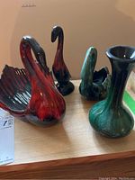 Four pottery items displayed on a table: two maroon swans, one turquoise swan, and a turquoise vase.