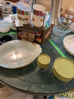 Overview of the lot on a green table showing the Pyrex containers with green lids, Pyrex oval baking dish with lid, and Matchables sugar and creamer set with floral motif in a box.