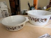 Two white Pyrex bowls with brown floral vine pattern shown side by side on a table.