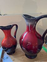 Front view of two large red and dark blue ceramic pitchers showing glazing and shape