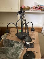 Overall view of the black hanging chandelier with three arms and hanging chain on cardboard surface.