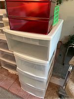 Photo showing white plastic storage drawers with two red metal tin boxes and a small green plastic organizer on top.