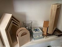 Wide view of shelf with nested wooden frames, wooden caddy, glass measuring cup, ceramic coasters, and part of the mugs and saucepan