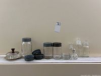 Full lot overview on white shelf against cream wall showing all jars, bottles, lids, pickle server, and lamp.