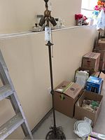 Full view of tall antique floor lamp with cast iron base standing near wall and surrounded by household items.