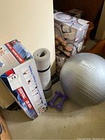 A yoga lot with a silver Body Sculpture exercise ball, purple dumbbells, gray rolled mat, and a boxed yoga set.
