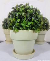 Front and partial side view of the ceramic pot with dense faux greenery on a white surface.