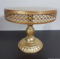 Front angle view of the gold-tone metal cake stand showing its lattice side design and solid top surface.