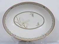 Oval serving bowl displayed on clear stand showing floral design and decorative border