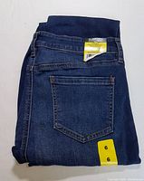 Folded dark blue denim jeans with elastic waistband fully visible, back pocket apparent with yellow Buffalo David Bitton label and size 6 sticker.