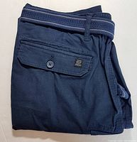Folded navy blue cargo shorts with visible button flap pocket and blue fabric belt with white stripes.