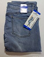 Folded light blue denim jeans showing back pocket and original tags with branding and sizing information.