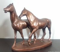 Front angle view of two bronze tone horses on oval base, showing details of horses' heads and bodies.