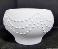 Side view of white ceramic bowl showing pearl relief decoration draped in garland style.