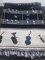 Folded cotton blanket showing white musical notes from Beethoven's Fifth Symphony on a black background with a white border of musical instrument silhouettes and fringed edges.