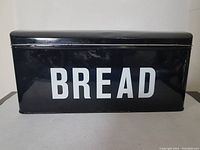 Front view of the rectangular black metal bread box showing large white BREAD text.