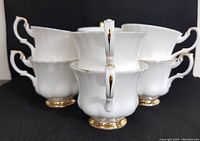 Photo showing the handles of the eight white bone china Royal Albert teacups with gold accents on the feet and handle tips, arranged in a stacked formation.